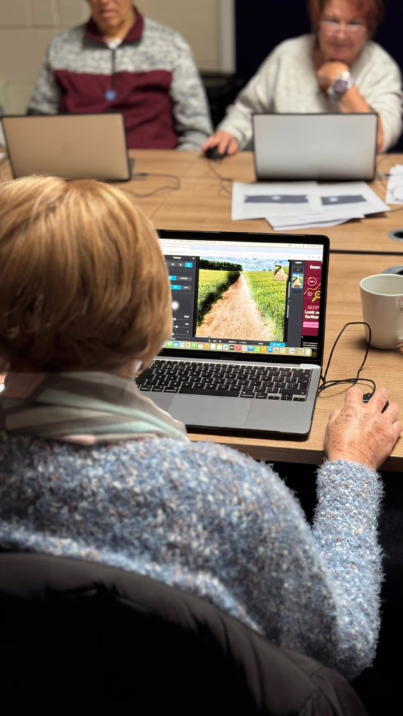 A group of senior adults sits at a table using laptops, with one woman editing a landscape photo using Pixlr.